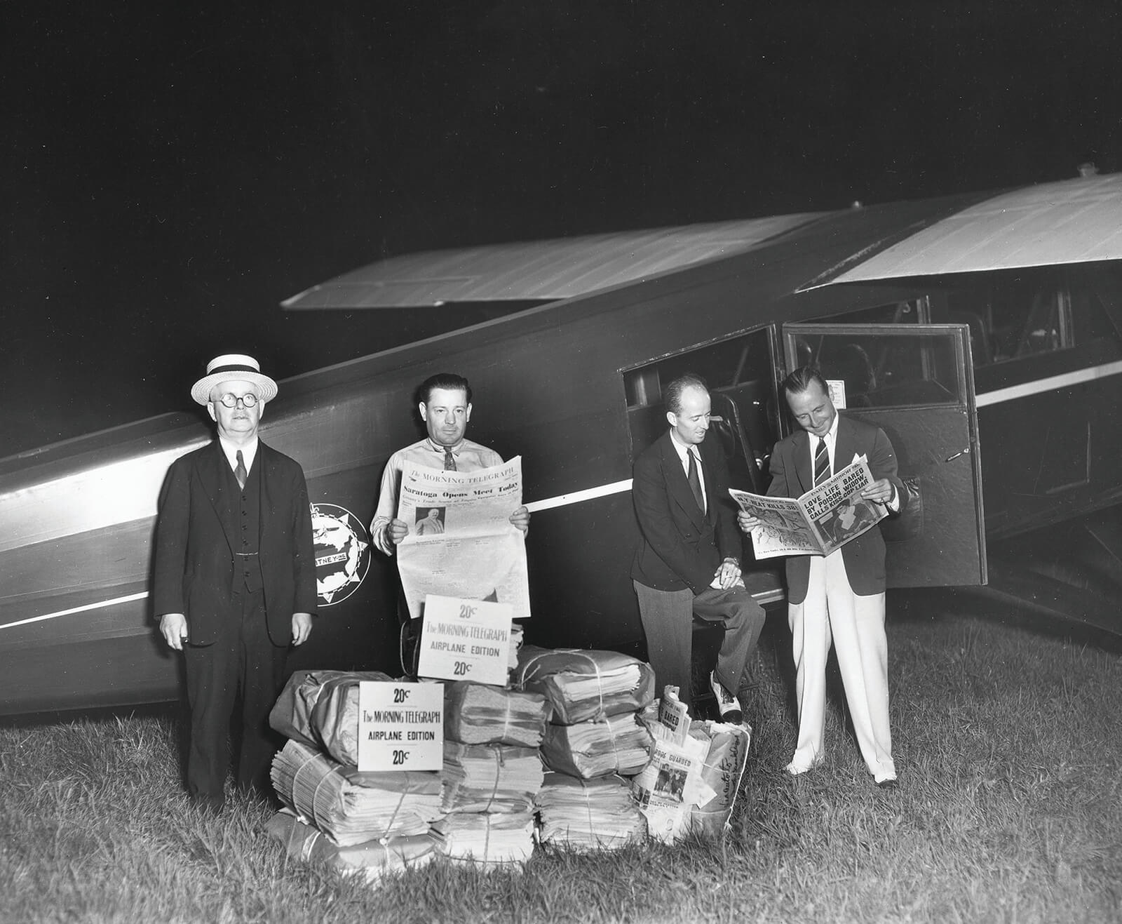 Men reading newspaper in front of airplane at Pitney Meadows Farm